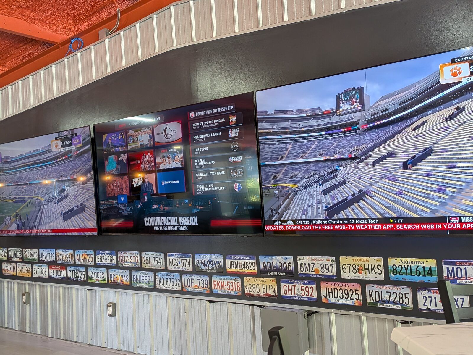 A wall of large screens showing sports above a row of vintage licence plates at Platform 32.